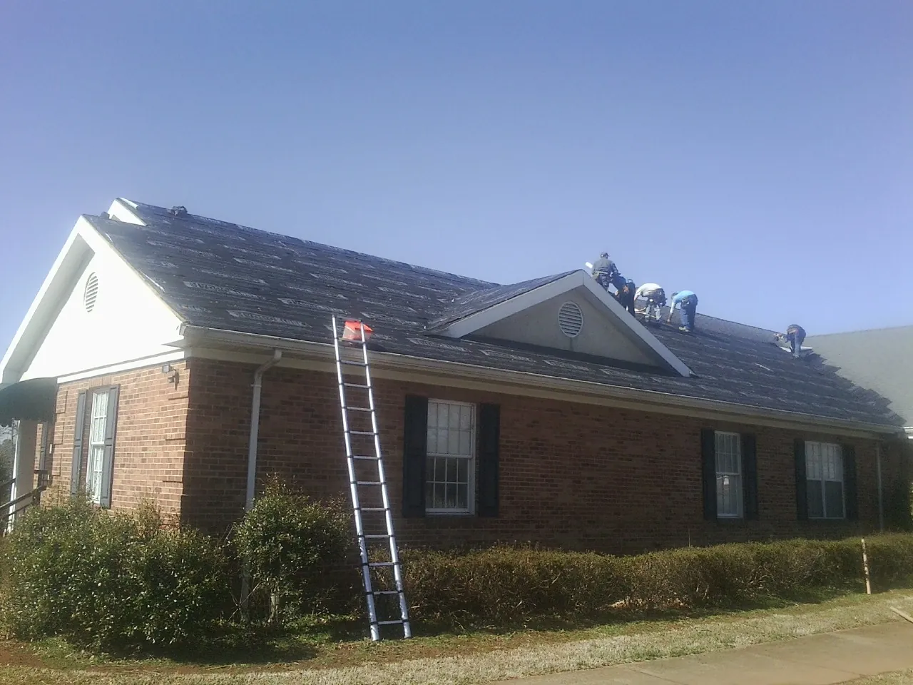 Crew tearing shingles off a brick ranch roof with a ladder set — Emergency Roof Repair work by our crew in Colton